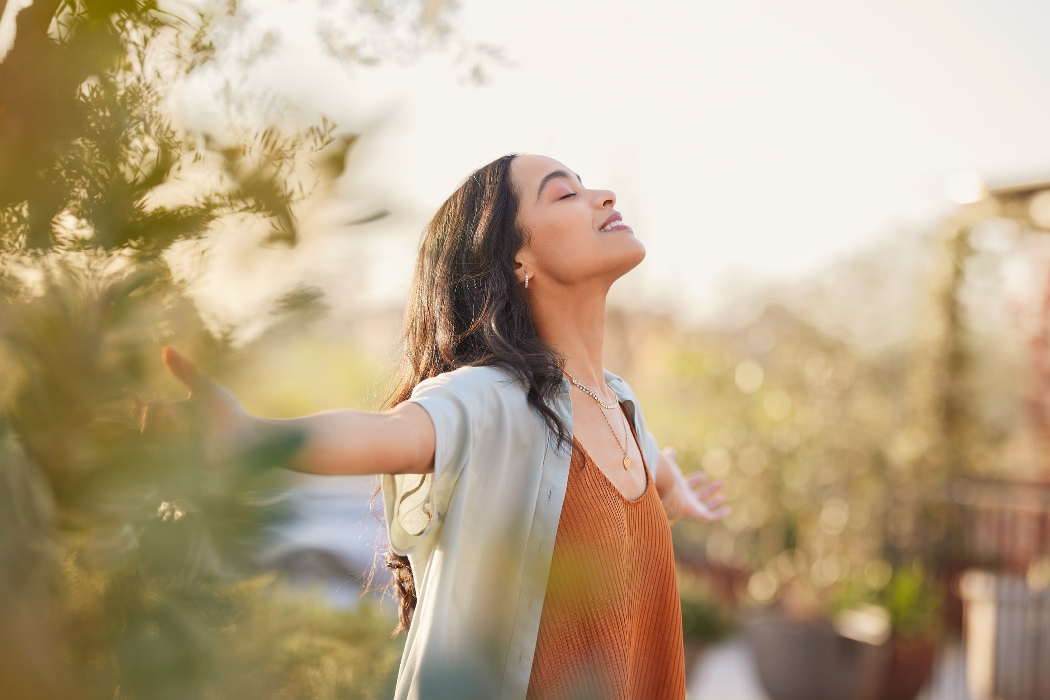 woman outdoors, smiling with arms outstretched and eyes closed